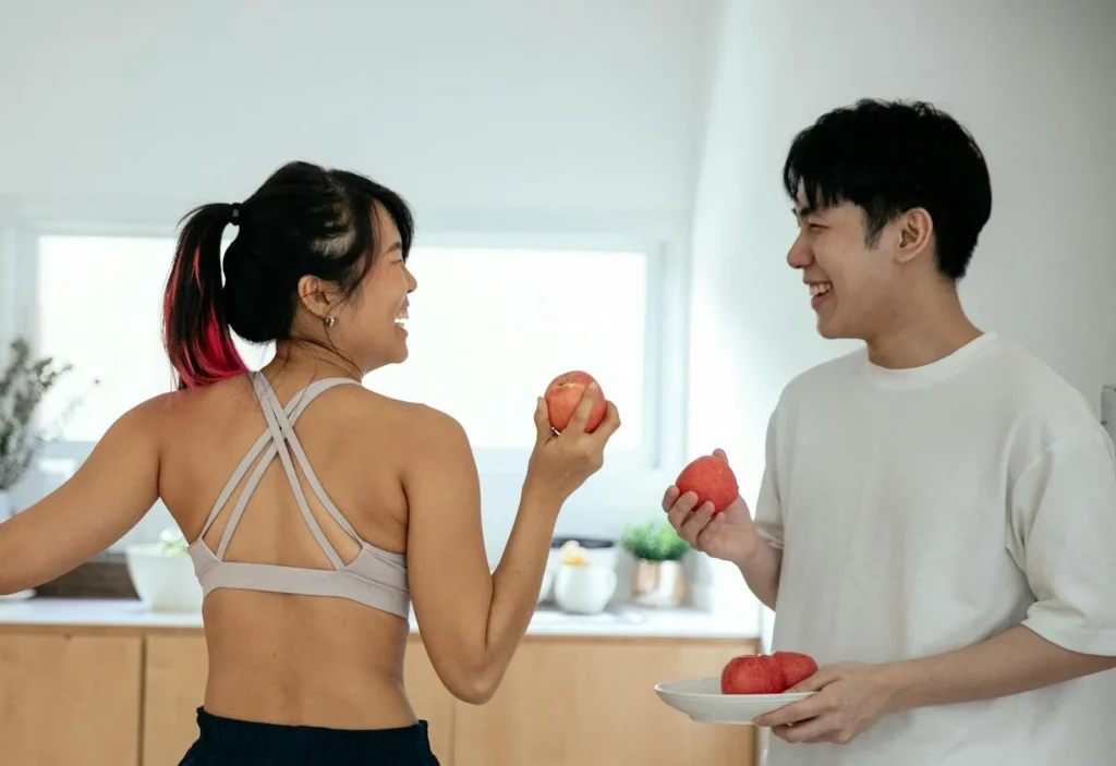 Asian couple enjoying fresh apples indoors, smiling and facing each other.